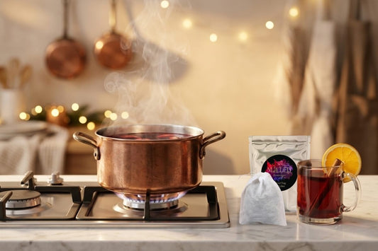 Mulled Beverages large spiced bag beside a steaming copper pot of mulled wine on a gas stove with a finished glass mug and orange slice