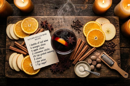 What is mulled wine guide with easy mulled wine recipe card surrounded by cinnamon sticks star anise cloves nutmeg orange slices and apple slices on a rustic wooden board